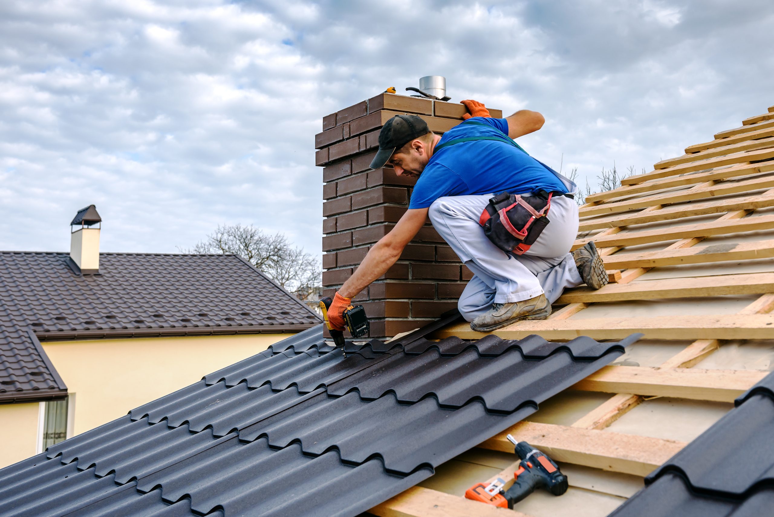 a professional master covers the roof Roofer in a blue shirt and white pants installing black metal panels on a sloped roof near a chimney. Tampa, FL
