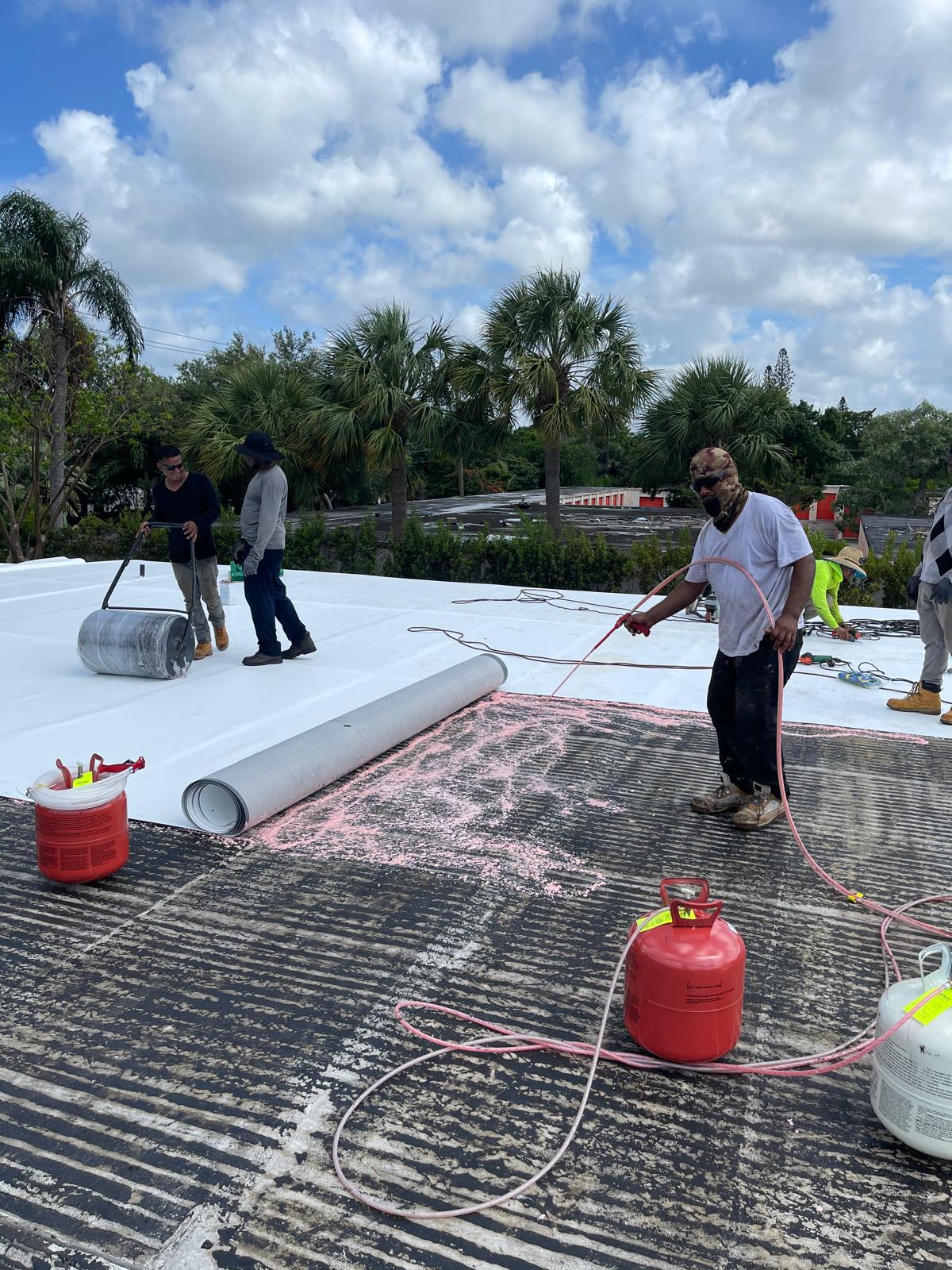 Four workers are installing roofing material with tools and gas canisters on a partially finished roof.