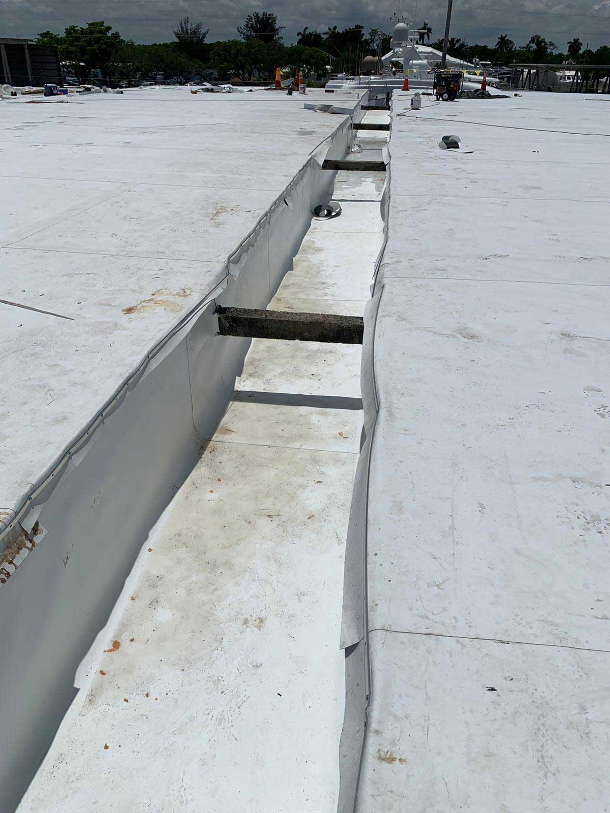 A long, narrow trench runs across a flat white rooftop under a cloudy sky.