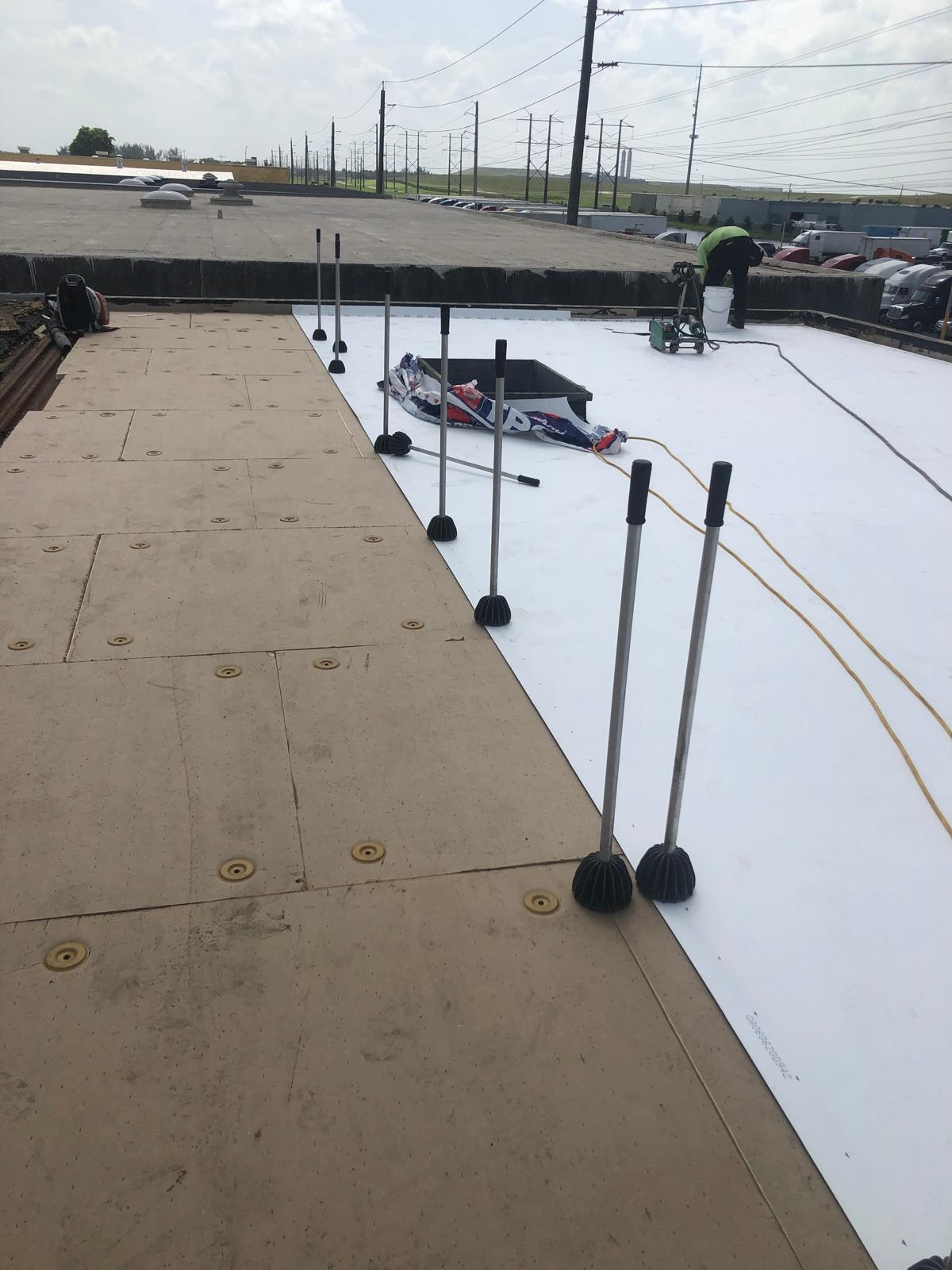 Workers installing white roofing membrane on a flat roof, with tools and materials spread out.