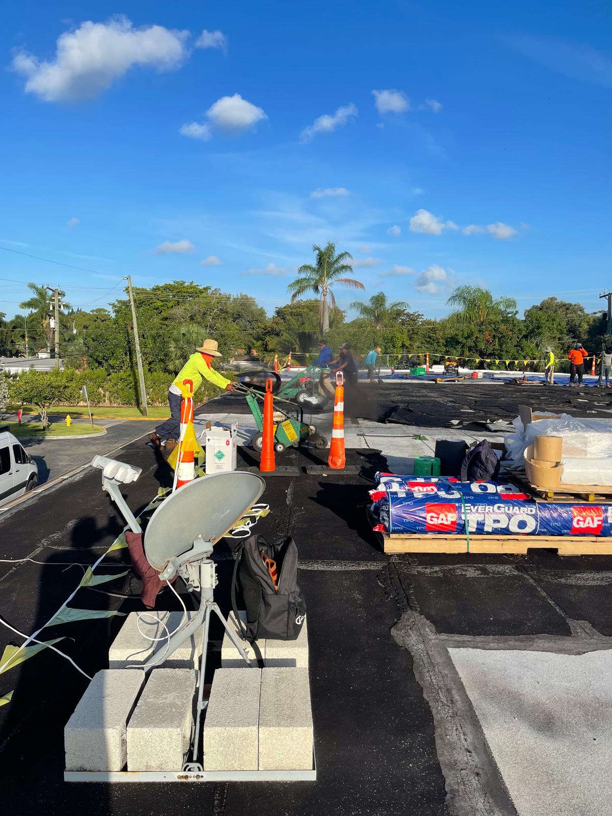 Workers in safety gear repairing a flat rooftop with equipment and materials under a clear blue sky.