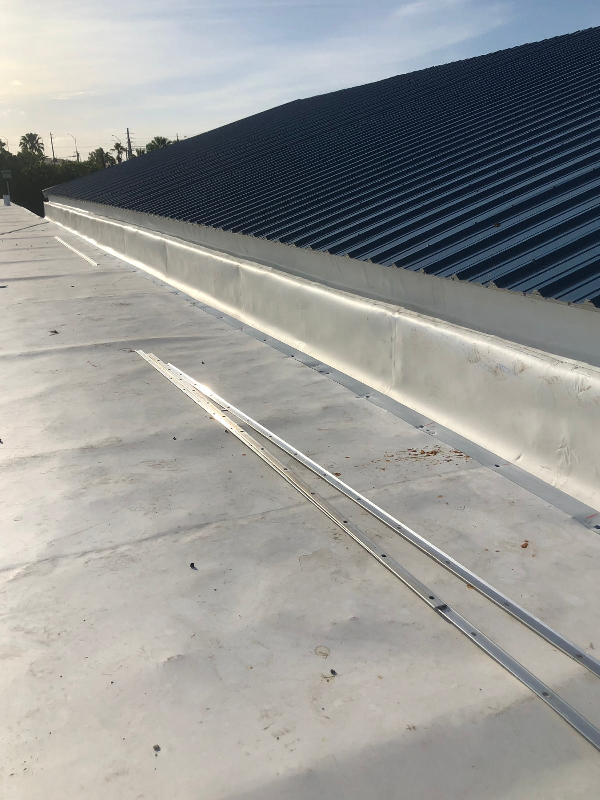 A rooftop with metal sheeting and a wide white membrane along the edge under a clear sky.