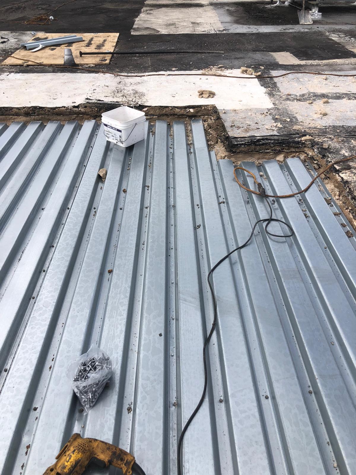 Corrugated metal roofing being installed, with tools, screws, and a wire visible on the roof surface.