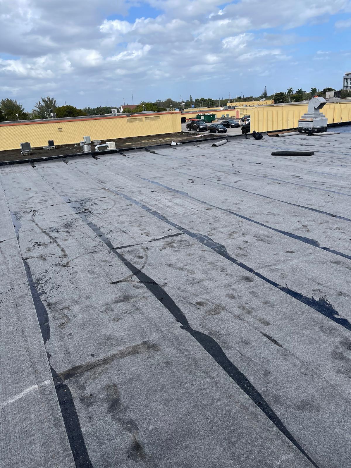 Flat commercial rooftop with grey waterproof membrane, HVAC units, and cloudy sky in the background.