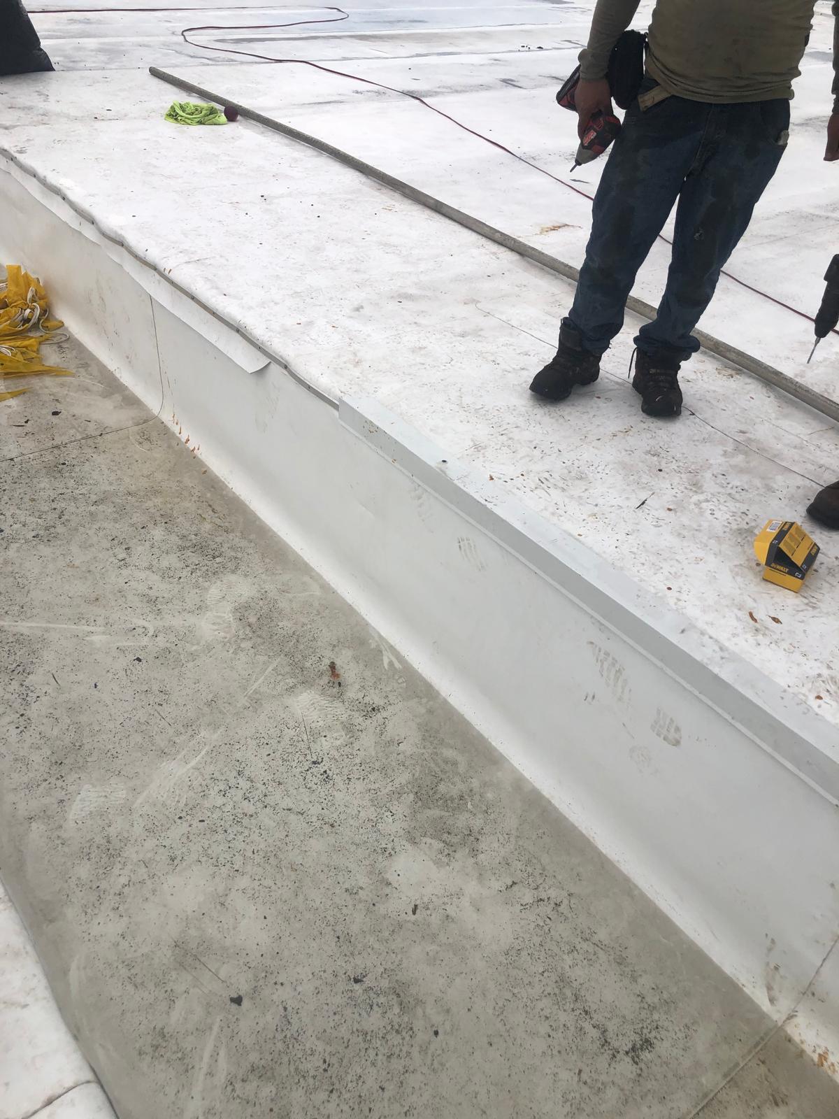 A person stands on a white surface next to an unfinished section, holding a tool with construction items nearby.