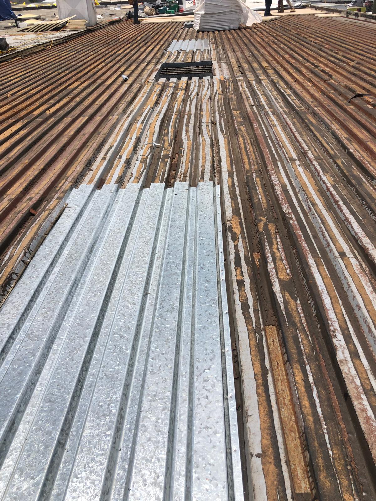 Corrugated metal sheets being installed on a wooden roof structure at a construction site.