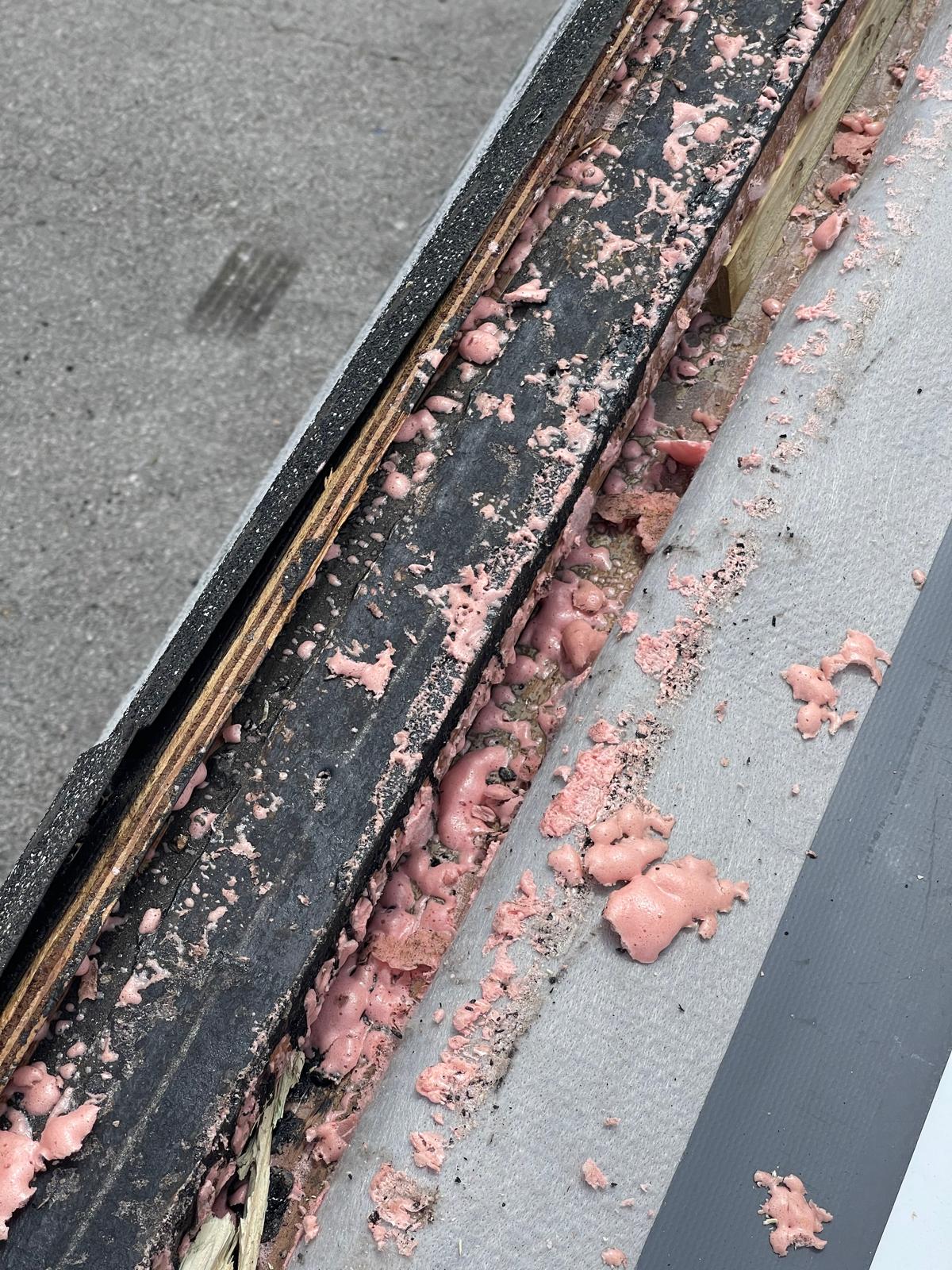 Close-up of pink insulation foam and weathered wood along the edge of a rooftop or outdoor surface.