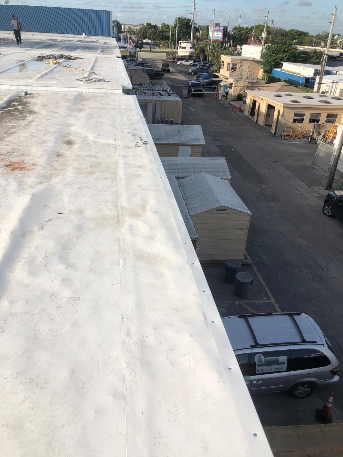 View from a rooftop looking down at parked cars, sheds, and buildings on a sunny day.