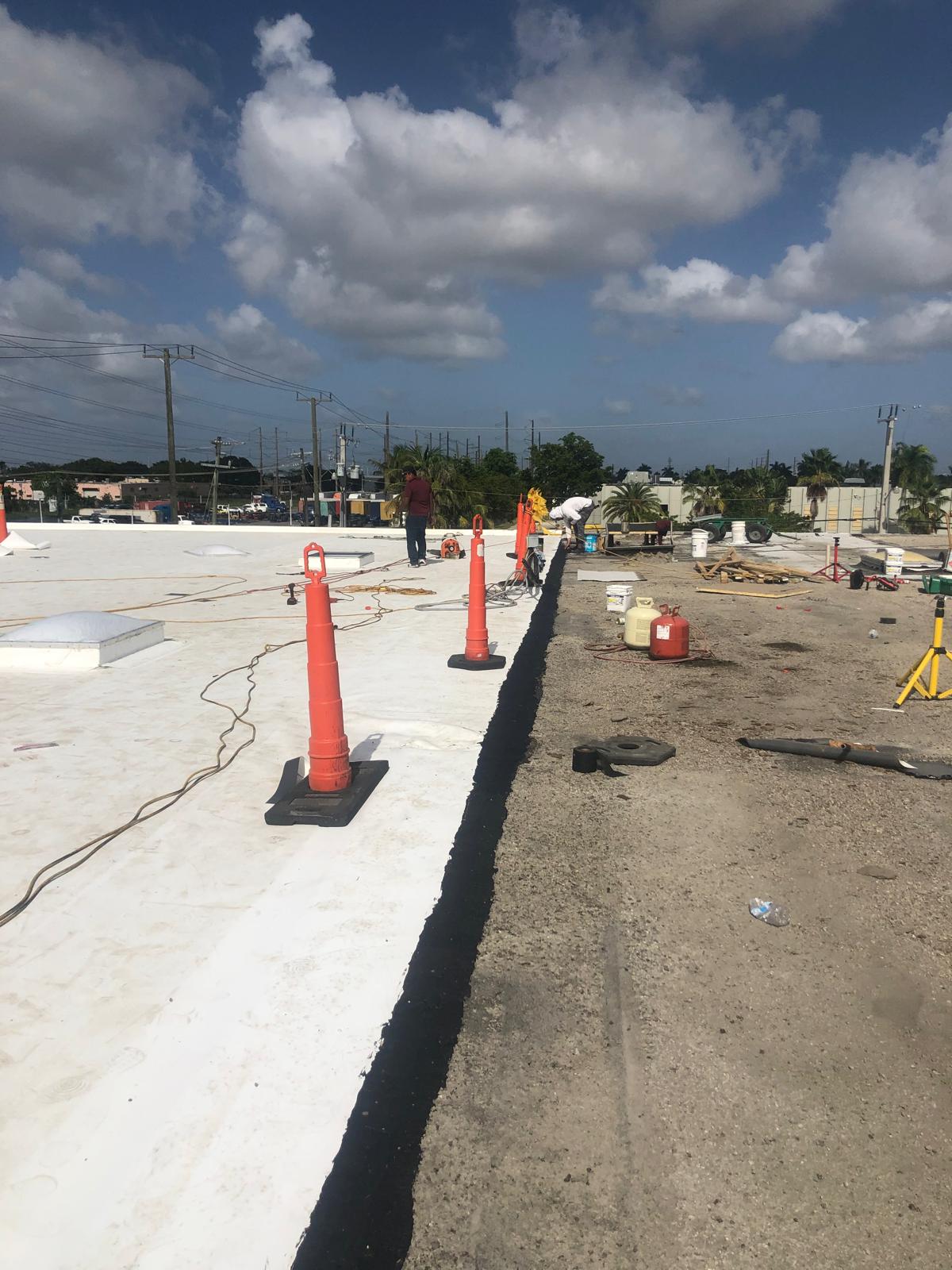 Workers on a construction site near traffic cones and equipment under a partly cloudy sky.