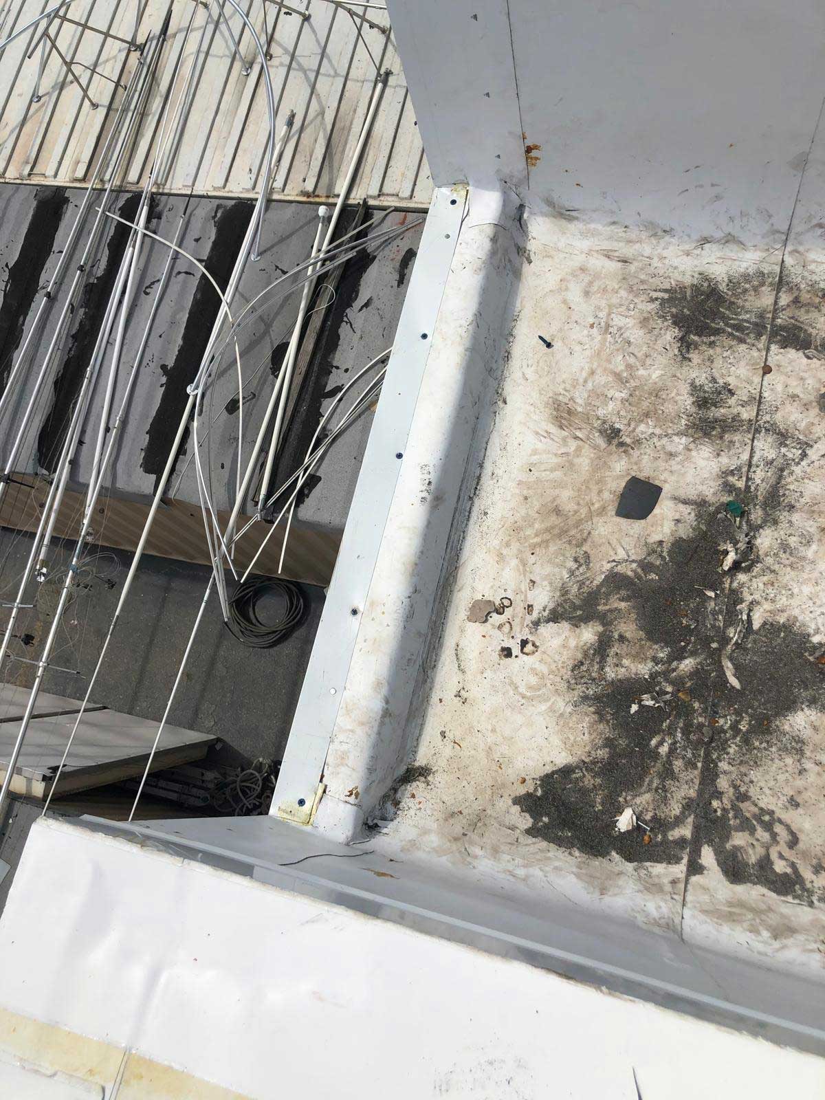 Rooftop view showing tangled wires, debris, and dirt on a white and gray surface.