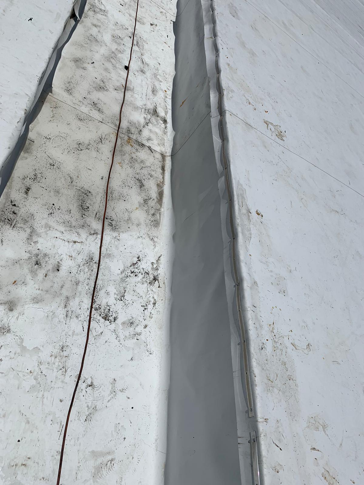 A white rooftop with a dirty section and a clean, raised seam running parallel to an orange cable.