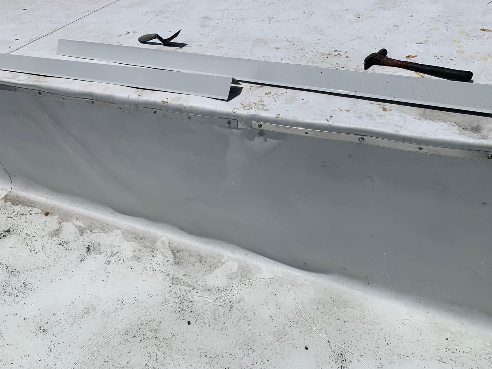 White metal flashing, tools, and a hammer on a flat rooftop with a light grey, fastened edge.