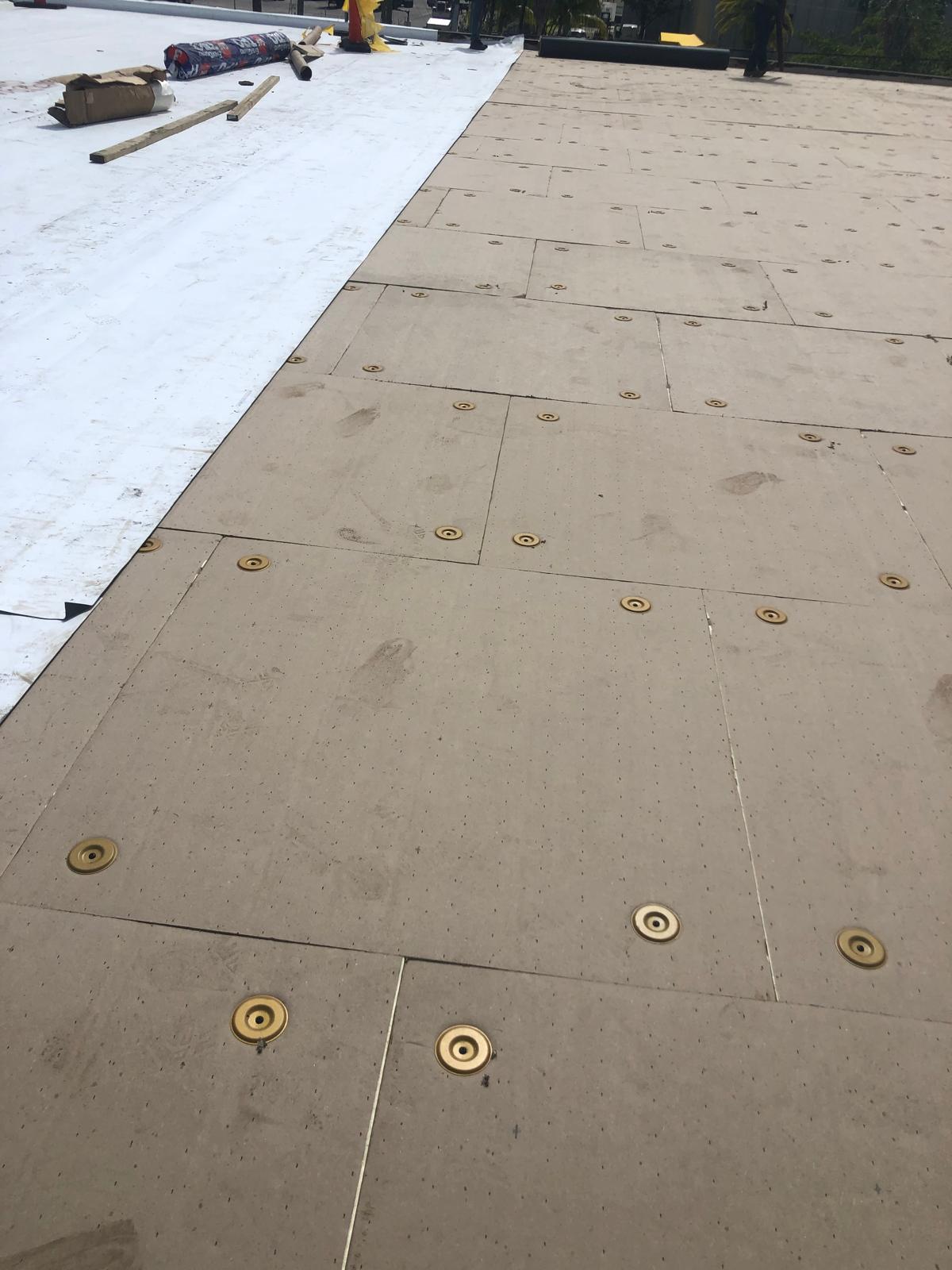 Close-up of roof insulation boards being installed, next to a section covered with white roofing membrane.