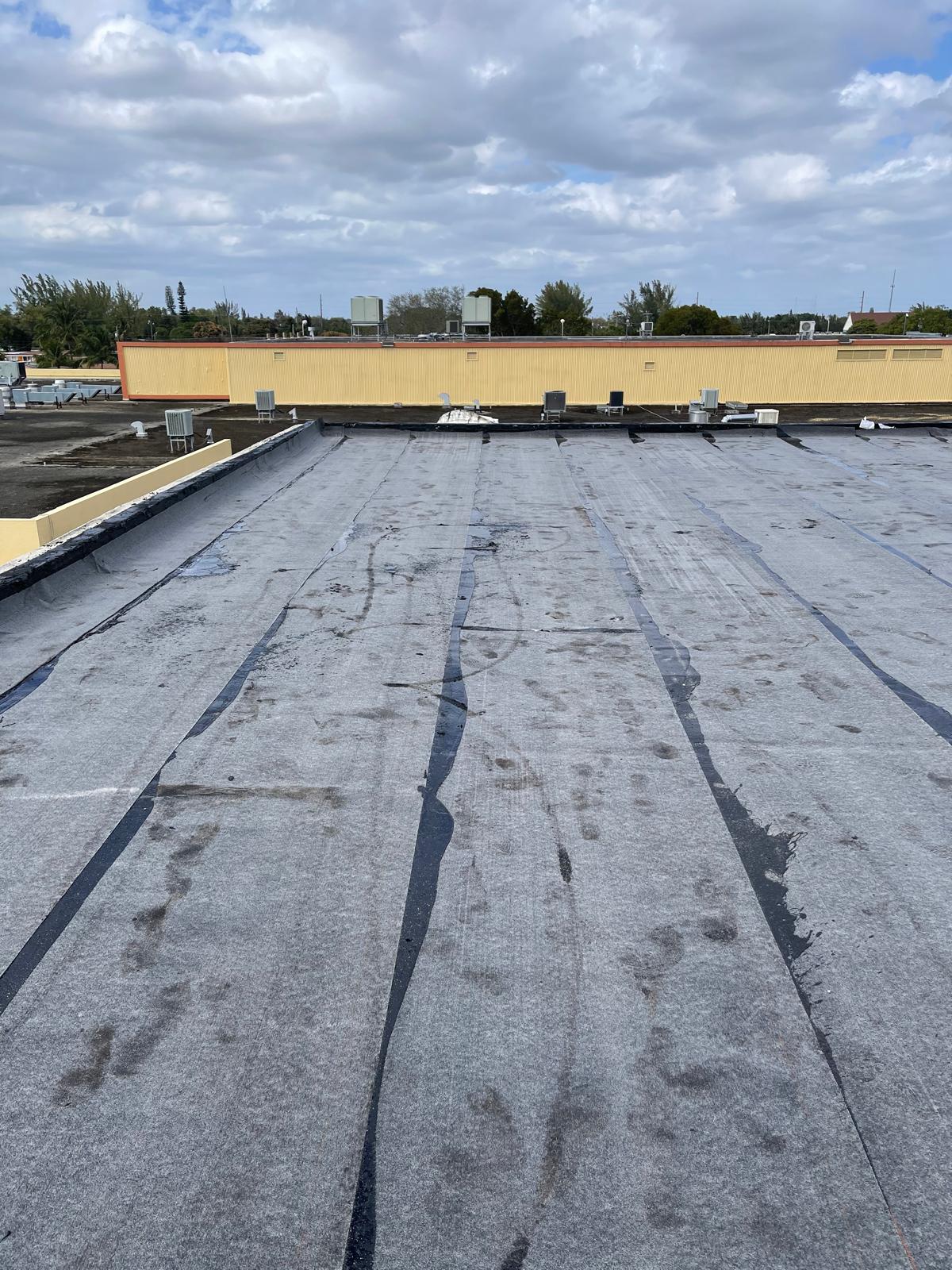 A flat commercial roof with black striping and water stains under a cloudy sky.