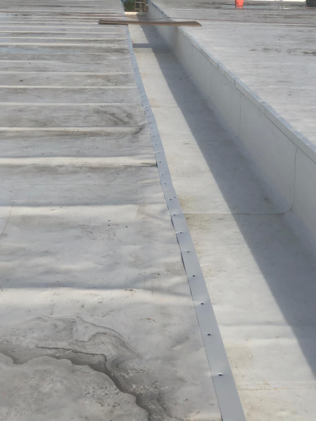 Flat white rooftop with metal edging and visible seams; some dirt and water stains are present on the surface.