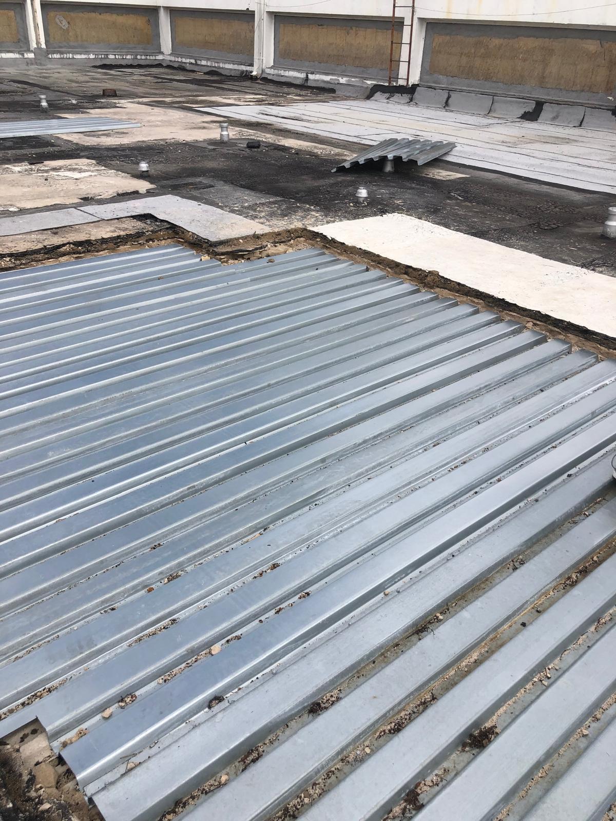 Corrugated metal roofing sheets laid out on a flat rooftop under construction or repair.