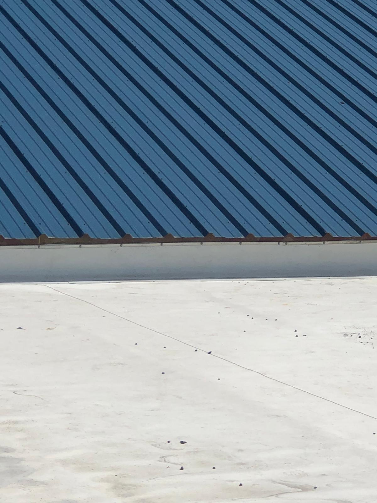 Blue metal roof with parallel ridges above a flat, light-colored concrete surface.