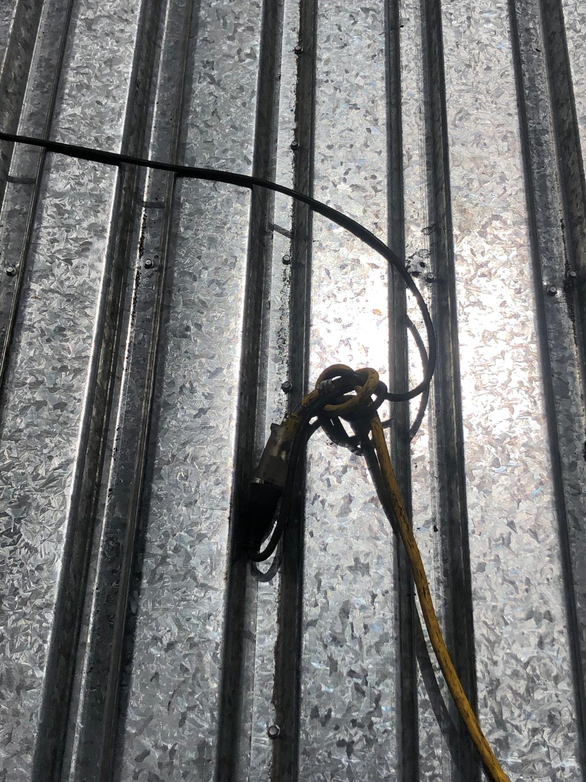 Black and yellow cables lying on a reflective corrugated metal surface in sunlight.