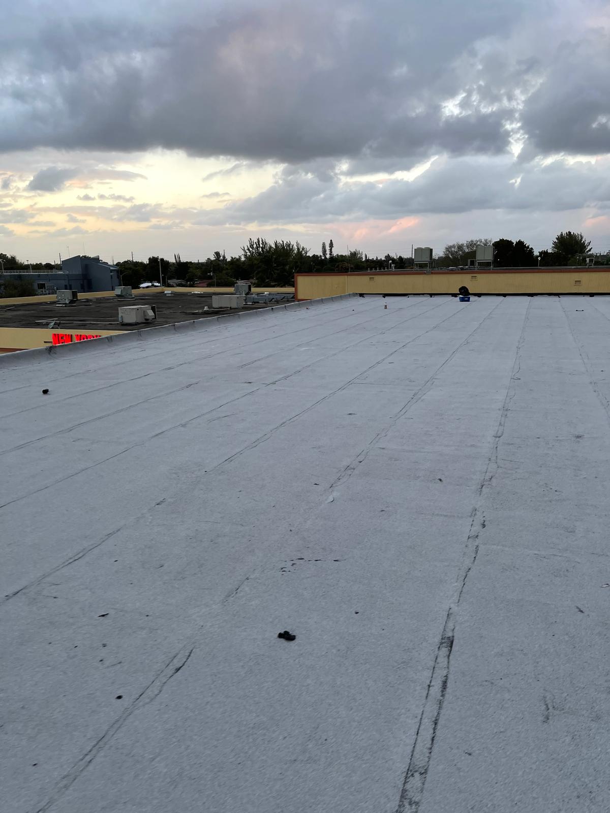 Flat rooftop with a few scattered objects, under a cloudy sky at sunset. Buildings and trees in the distance.
