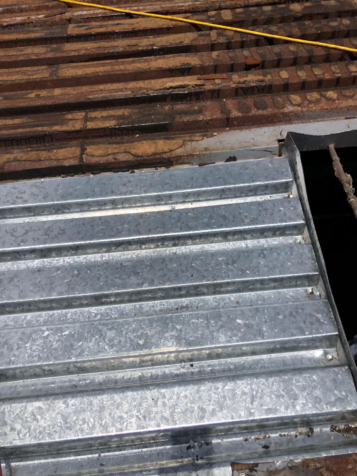 Corrugated metal sheet partially covering a roof with exposed wooden beams and a yellow cable.