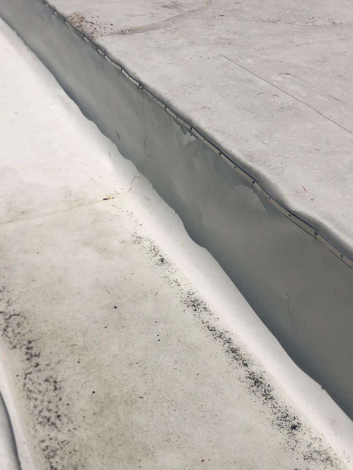 Close-up of a seam on a flat white rooftop with visible dirt and slight buckling in the material.