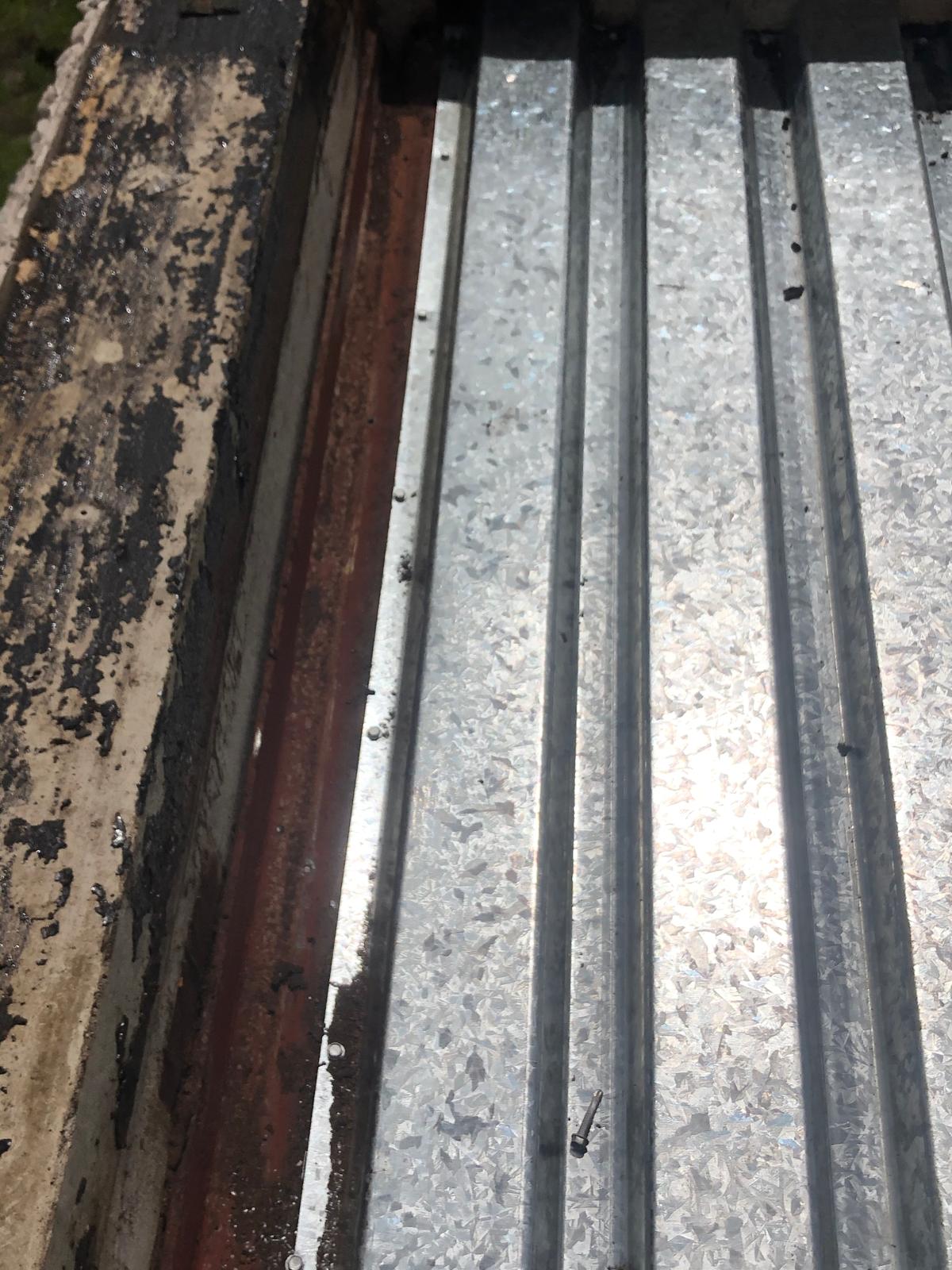 Rusty edge of a metal sheet roof with sunlight reflecting off its corrugated, silver surface.