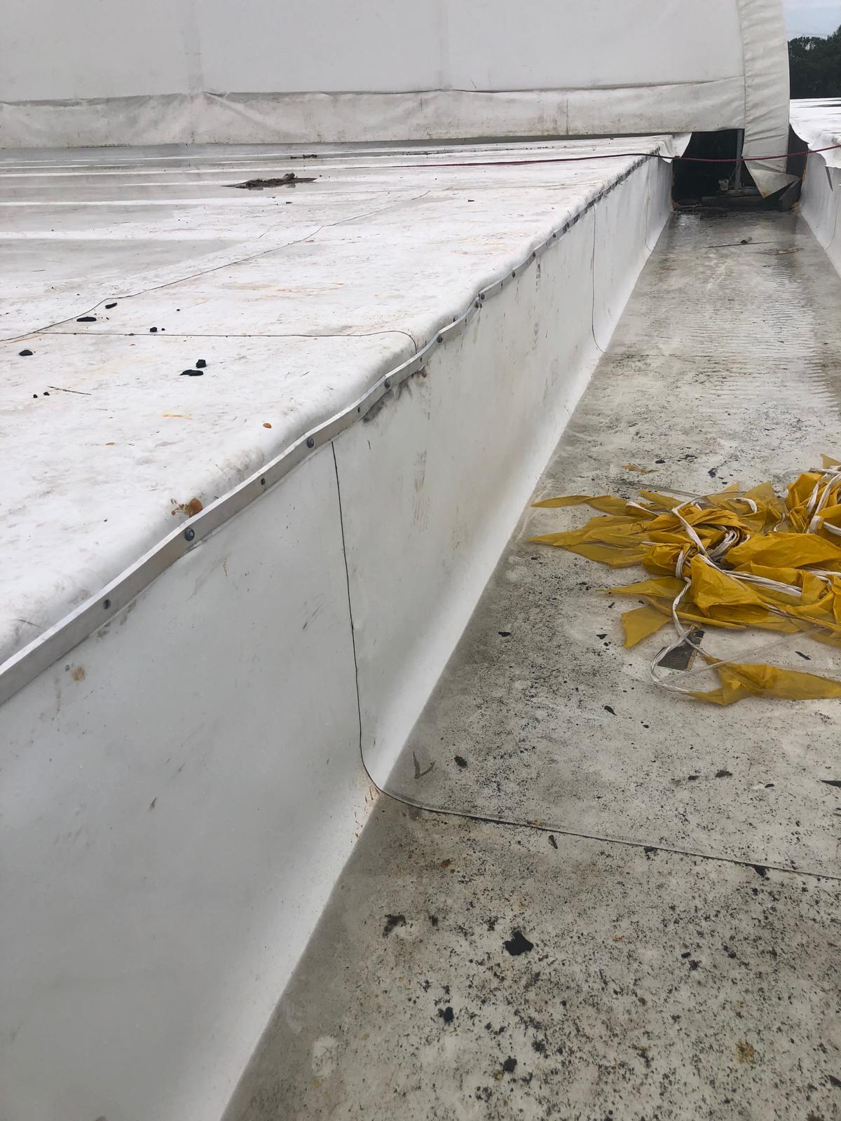 White industrial roof surface with some dirt, debris, and a pile of yellow straps on the right side.