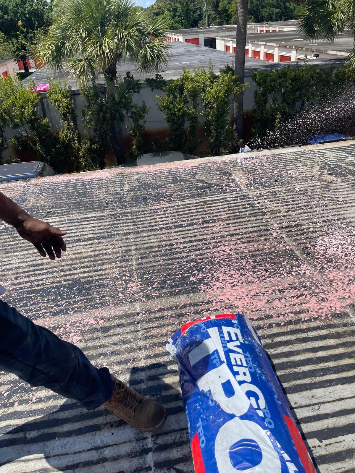 Person standing on a corrugated roof, spreading pink roofing material from an Everguard TPO package.