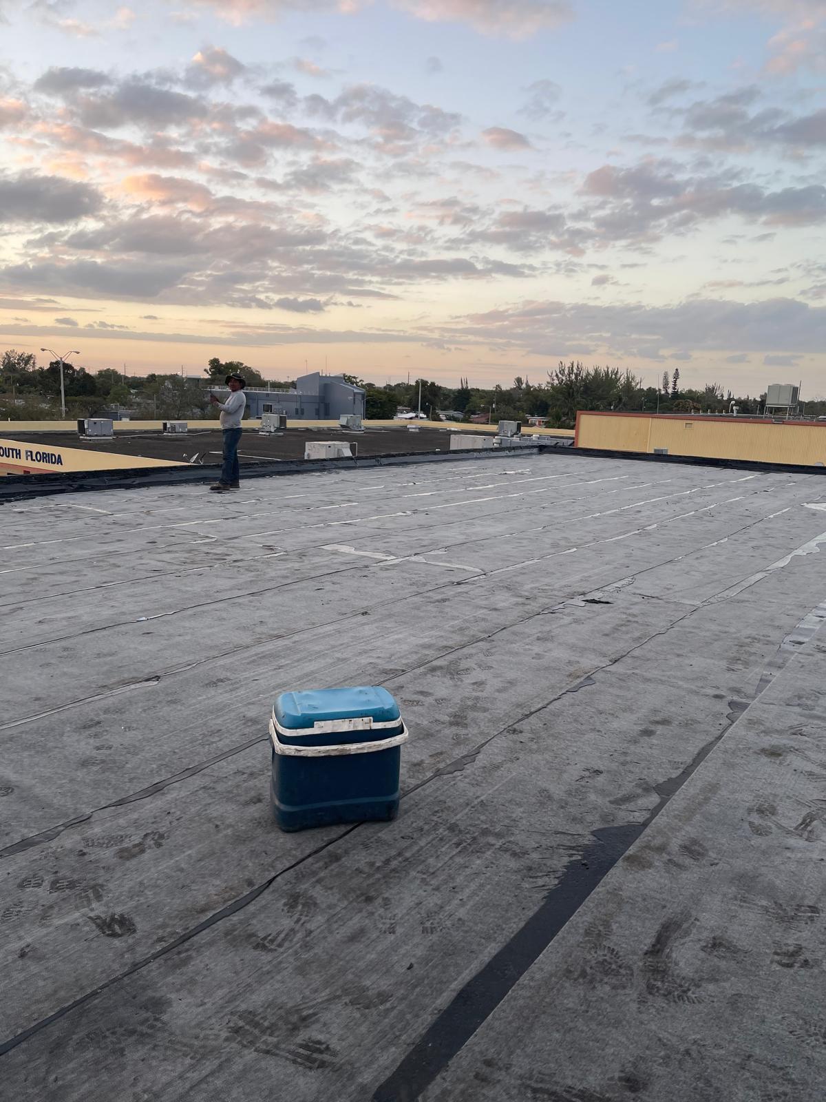 A person stands on a flat rooftop at sunset with a blue cooler in the foreground.
