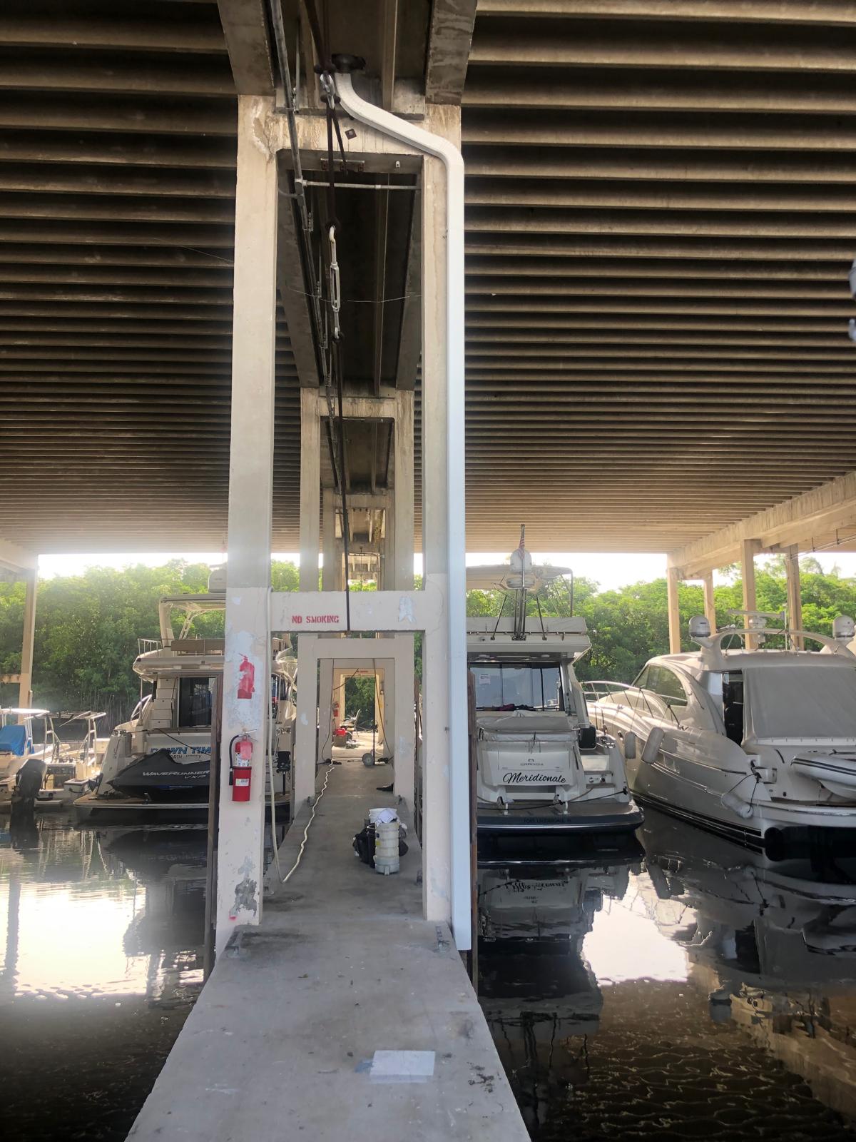 Dock walkway under a covered marina, with boats moored on both sides and safety equipment on the pillar.