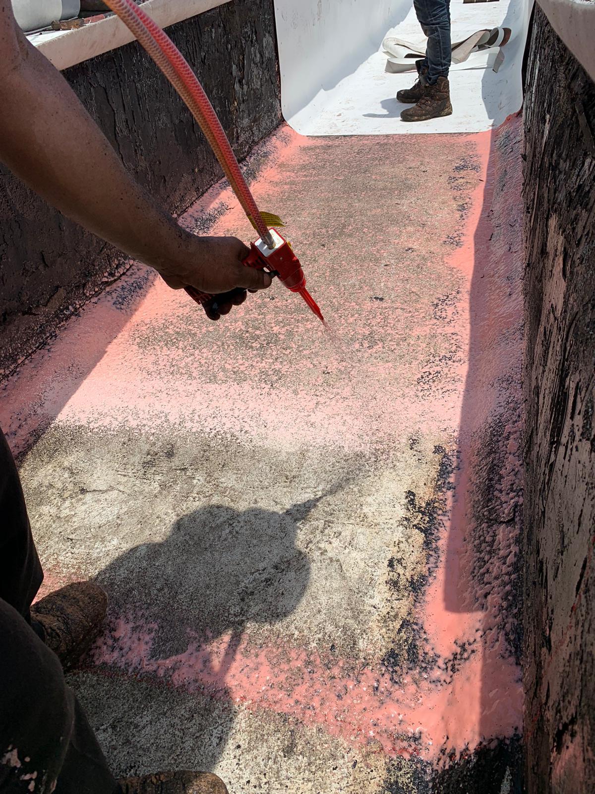 Person spraying pink liquid onto a rough surface, with another person standing in the background.
