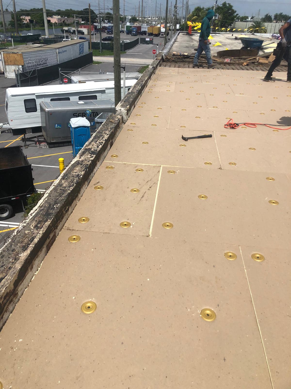 Wide view of a flat white rooftop under a partly cloudy sky, with construction materials scattered.