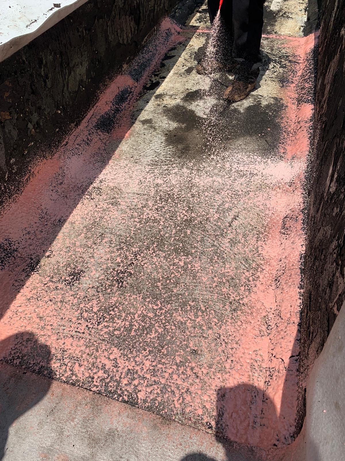 Person spreading pink powder on a flat, concrete surface with sunlight casting shadows.