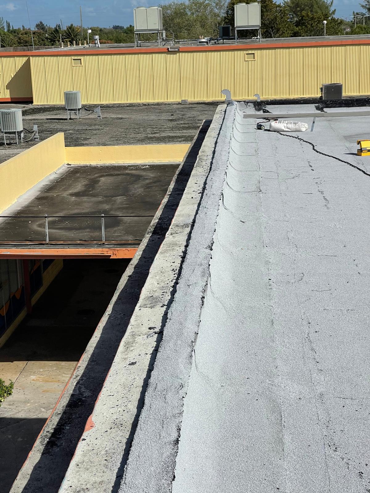 View of a flat, newly resurfaced white rooftop next to an older, darker roof on a commercial building.