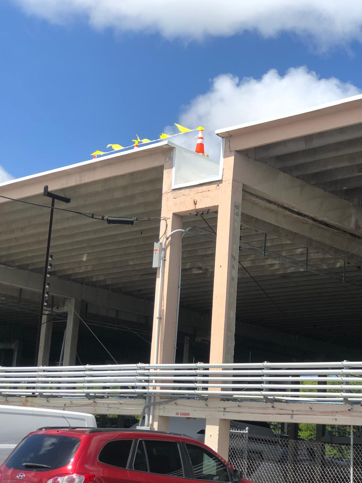 An orange traffic cone and yellow flags sit on the edge of a partially constructed parking garage roof.