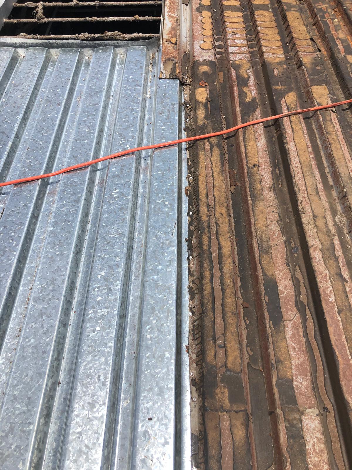 A new shiny metal roof panel beside an old, rusted corrugated metal sheet with an orange wire across.