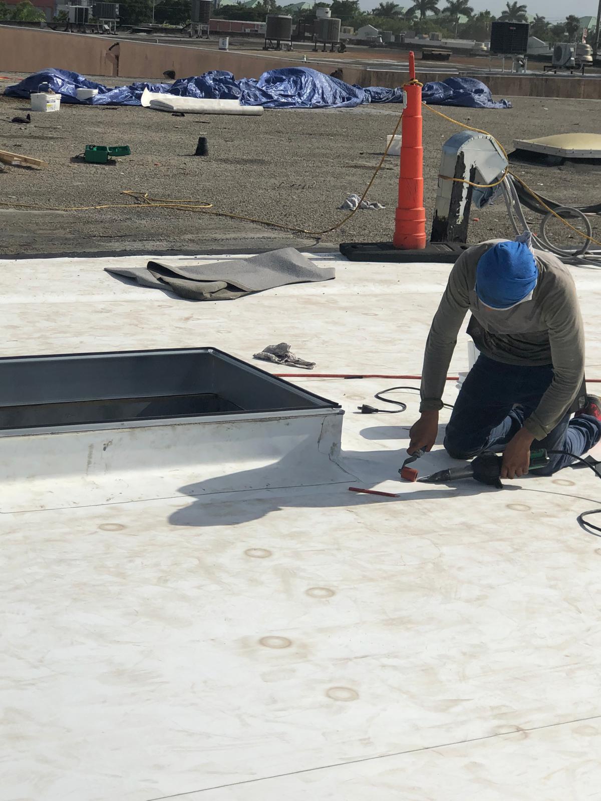Person in blue headscarf uses power tool on white rooftop, with equipment and materials nearby.