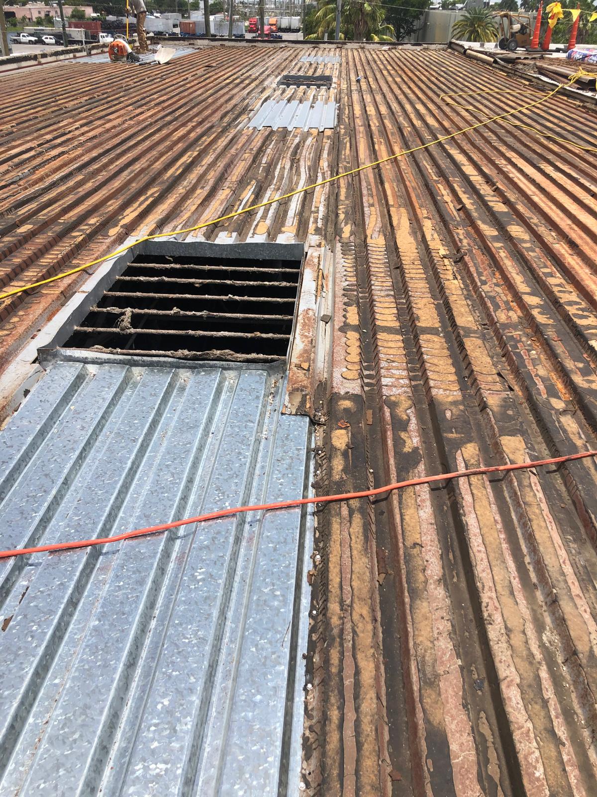 Corrugated metal roof with missing panels, exposed beams, and some new metal sheets being installed.