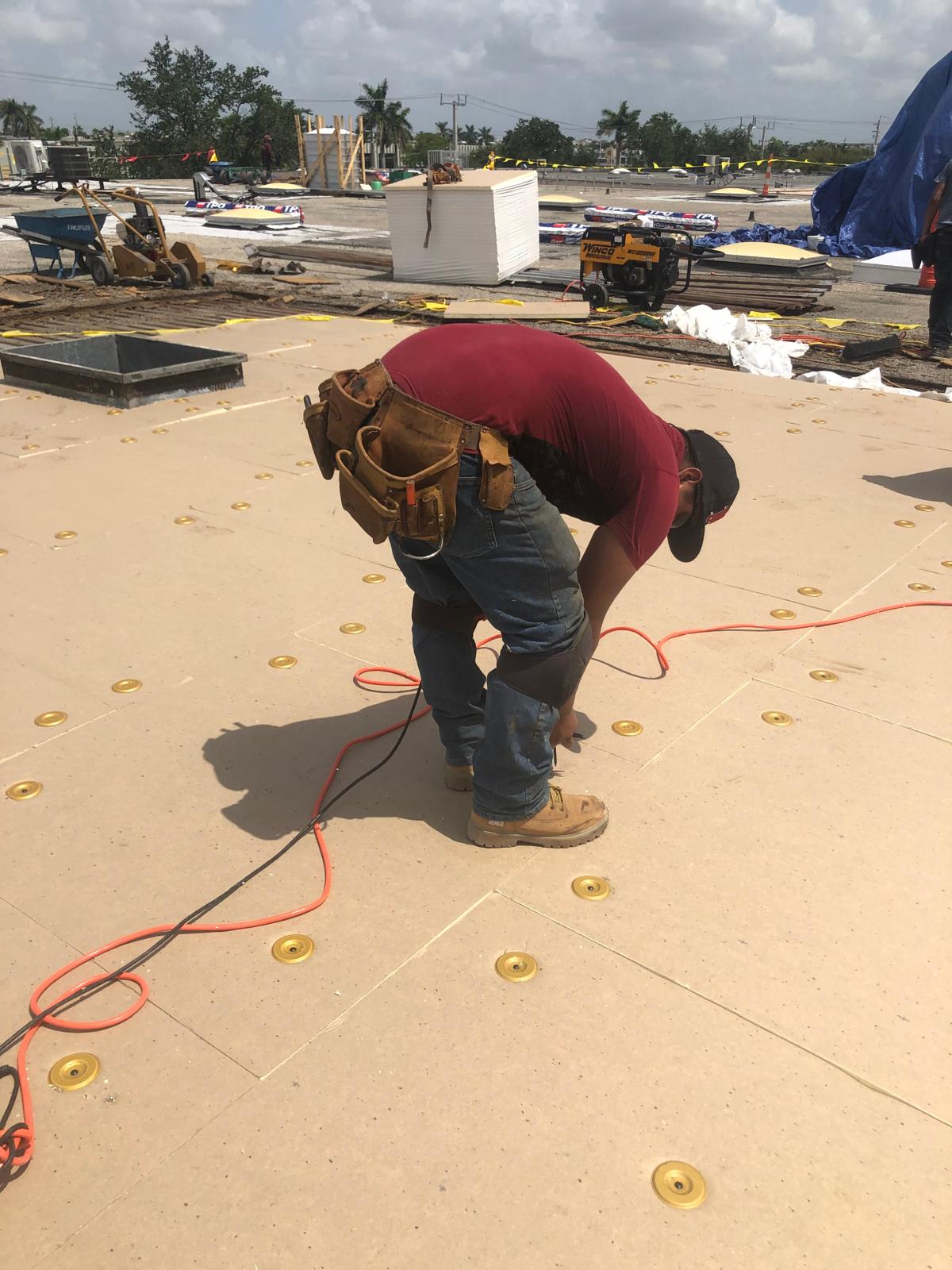 A construction worker bends over while working on a roof, surrounded by tools and construction materials.
