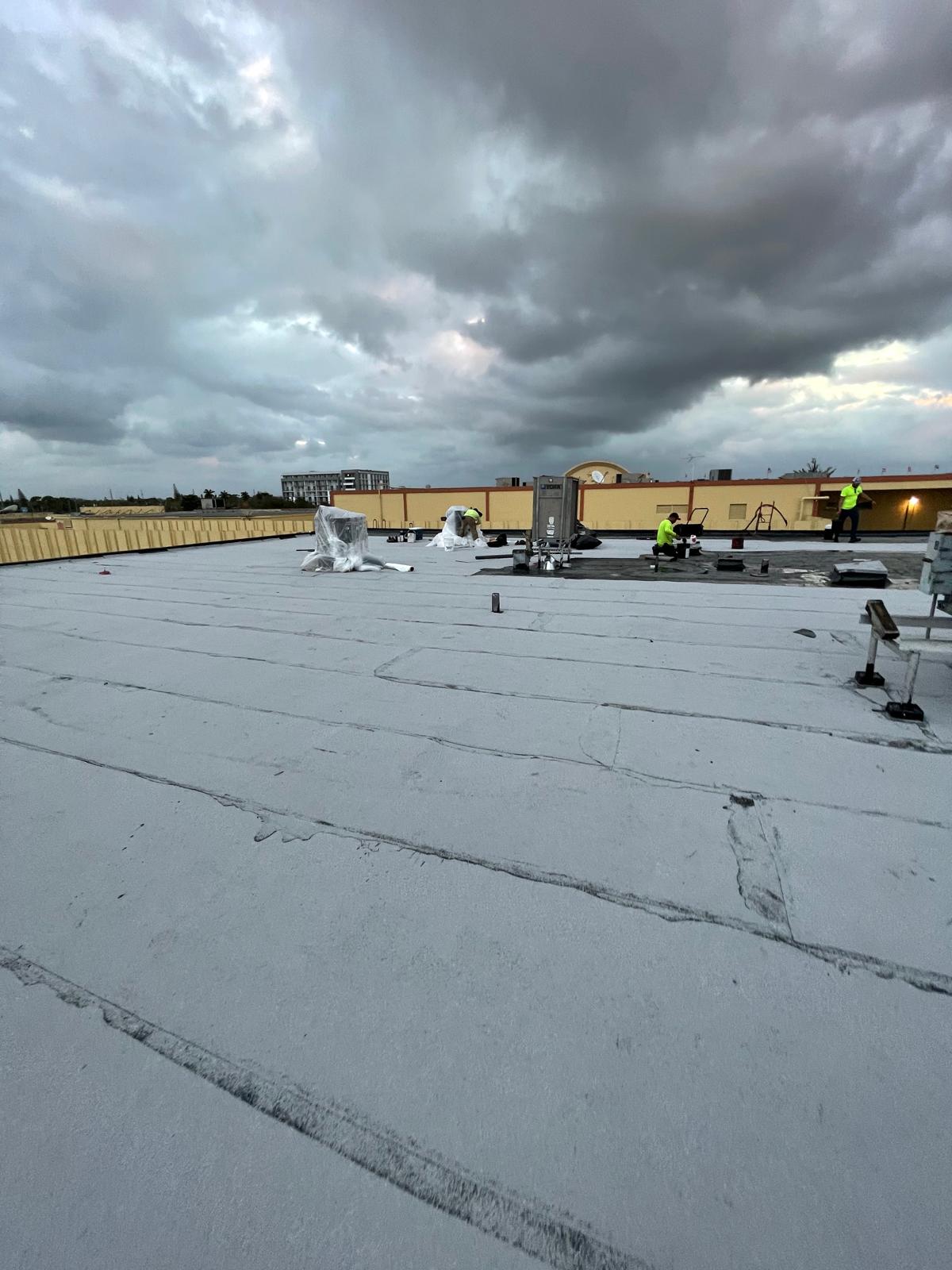 Workers on a flat rooftop under a cloudy sky, with equipment and materials scattered around.