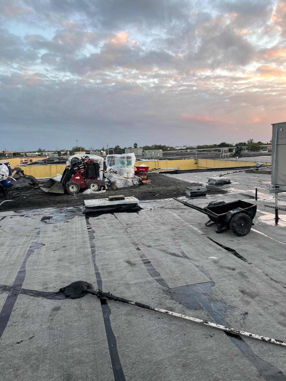 A rooftop construction site with equipment and materials under a cloudy sunset sky.