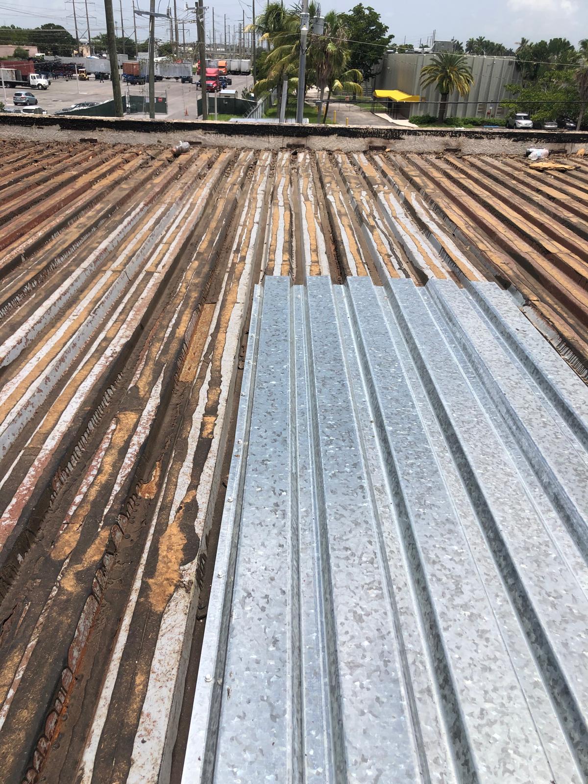 Corrugated metal sheets being installed on a rusted roof, with a parking lot and trees in the background.