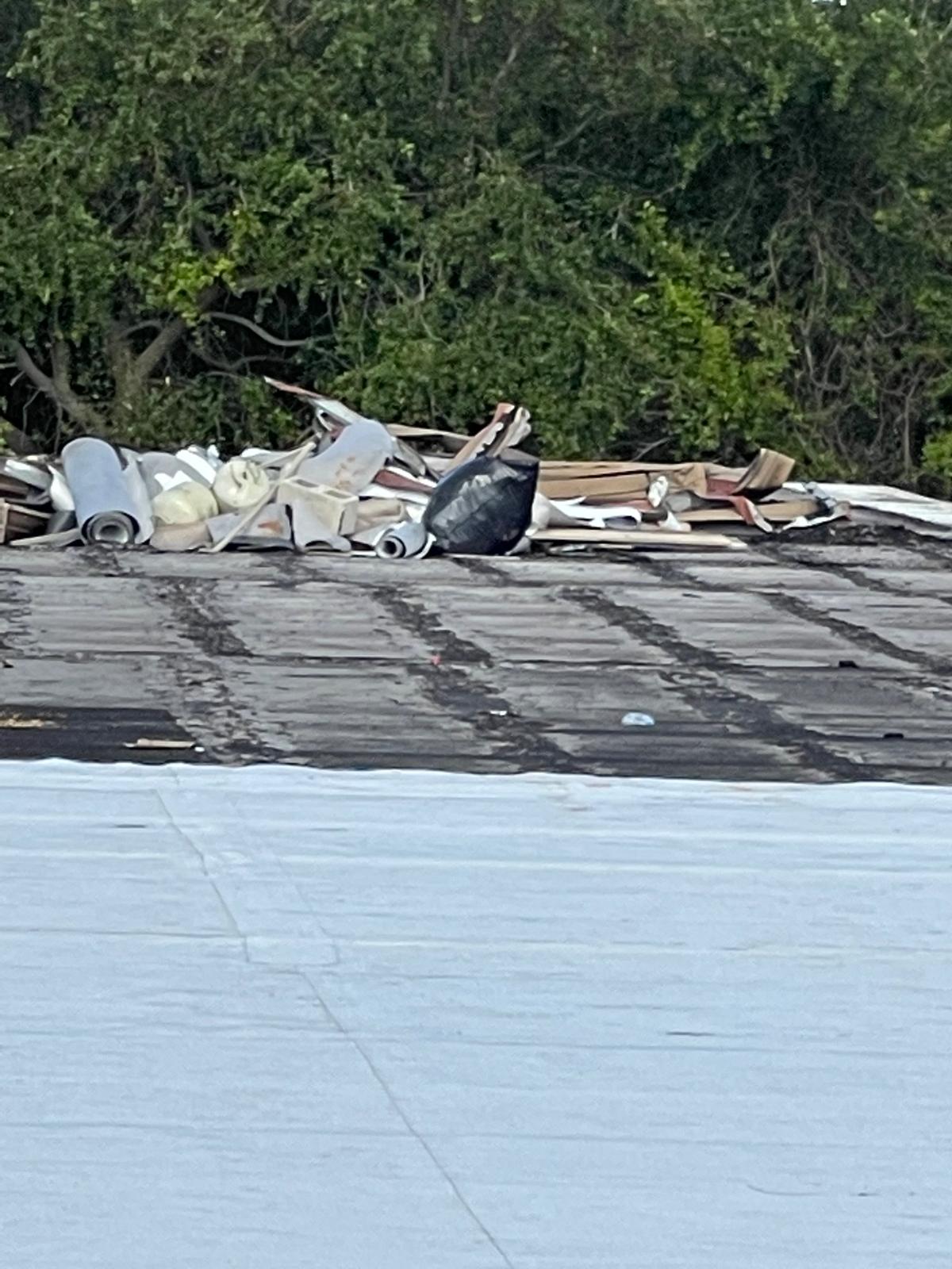 Rolled roofing materials and debris piled on a rooftop, with trees in the background.