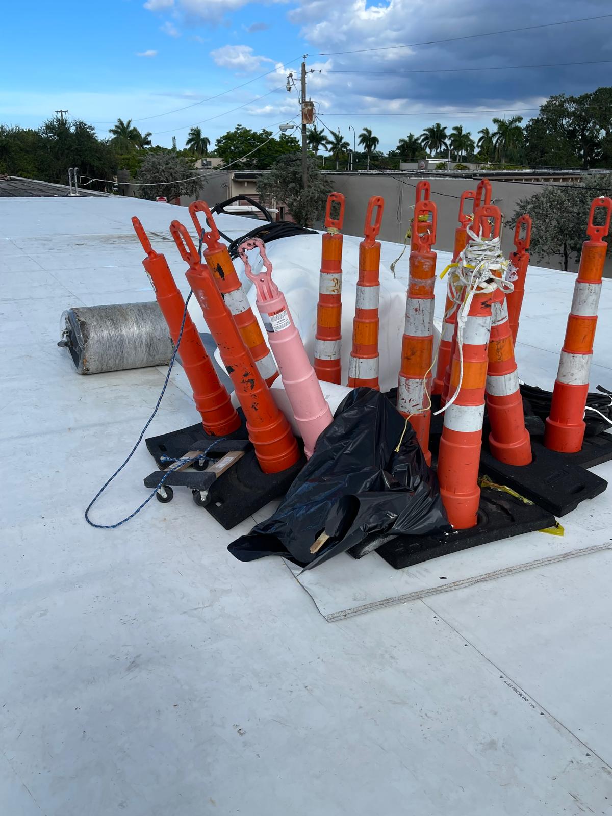 A group of orange traffic cones, some tied together, sit on a flat white rooftop with a black bag nearby.