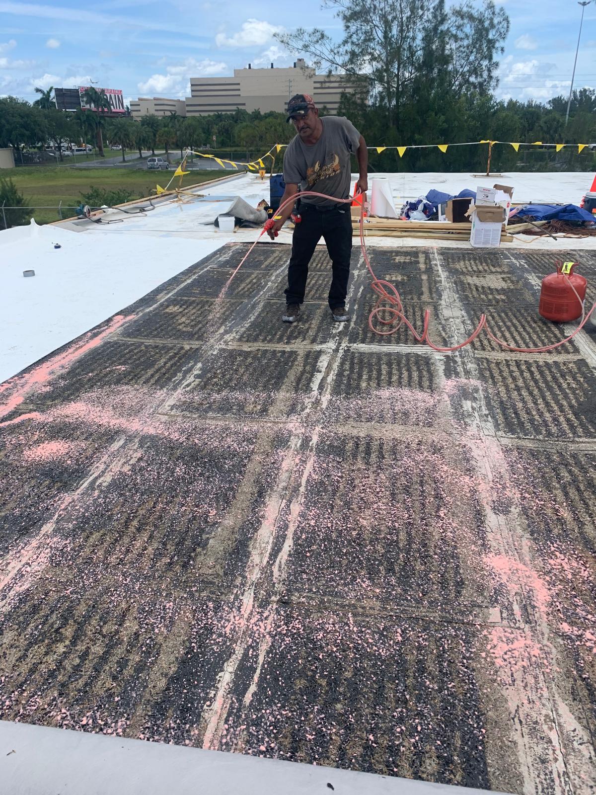 Man spraying pink paint on a rooftop under construction, with buildings and trees visible in the background.