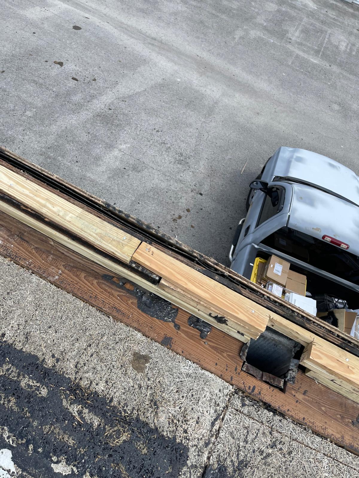 View from a roof showing wooden beams and a parked car loaded with boxes on a gray pavement below.
