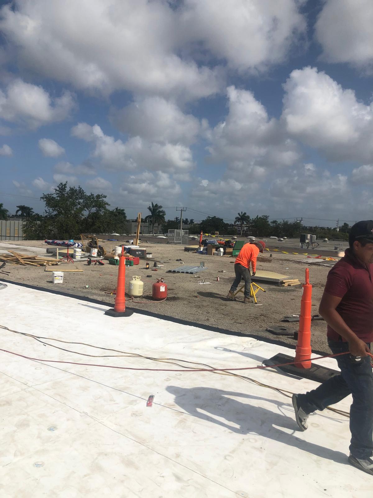 Construction workers and scattered tools on a rooftop work site under a partly cloudy sky.