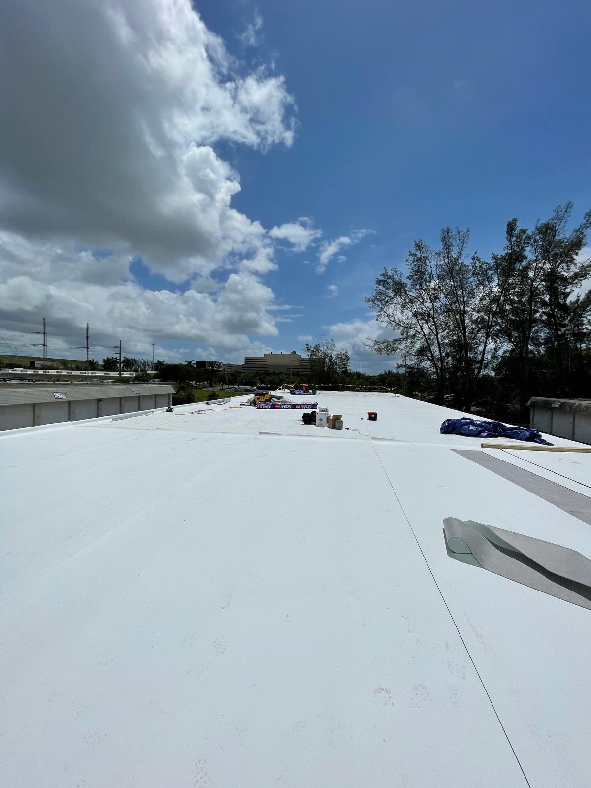 Wide view of a flat white rooftop under a partly cloudy sky, with construction materials scattered.