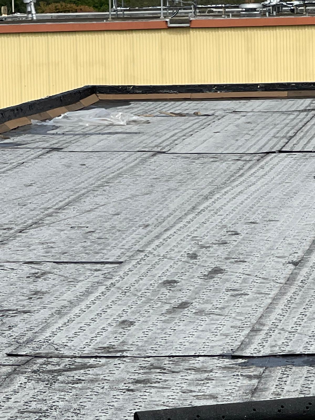 A flat rooftop with a textured, waterproof membrane and a yellow building wall in the background.