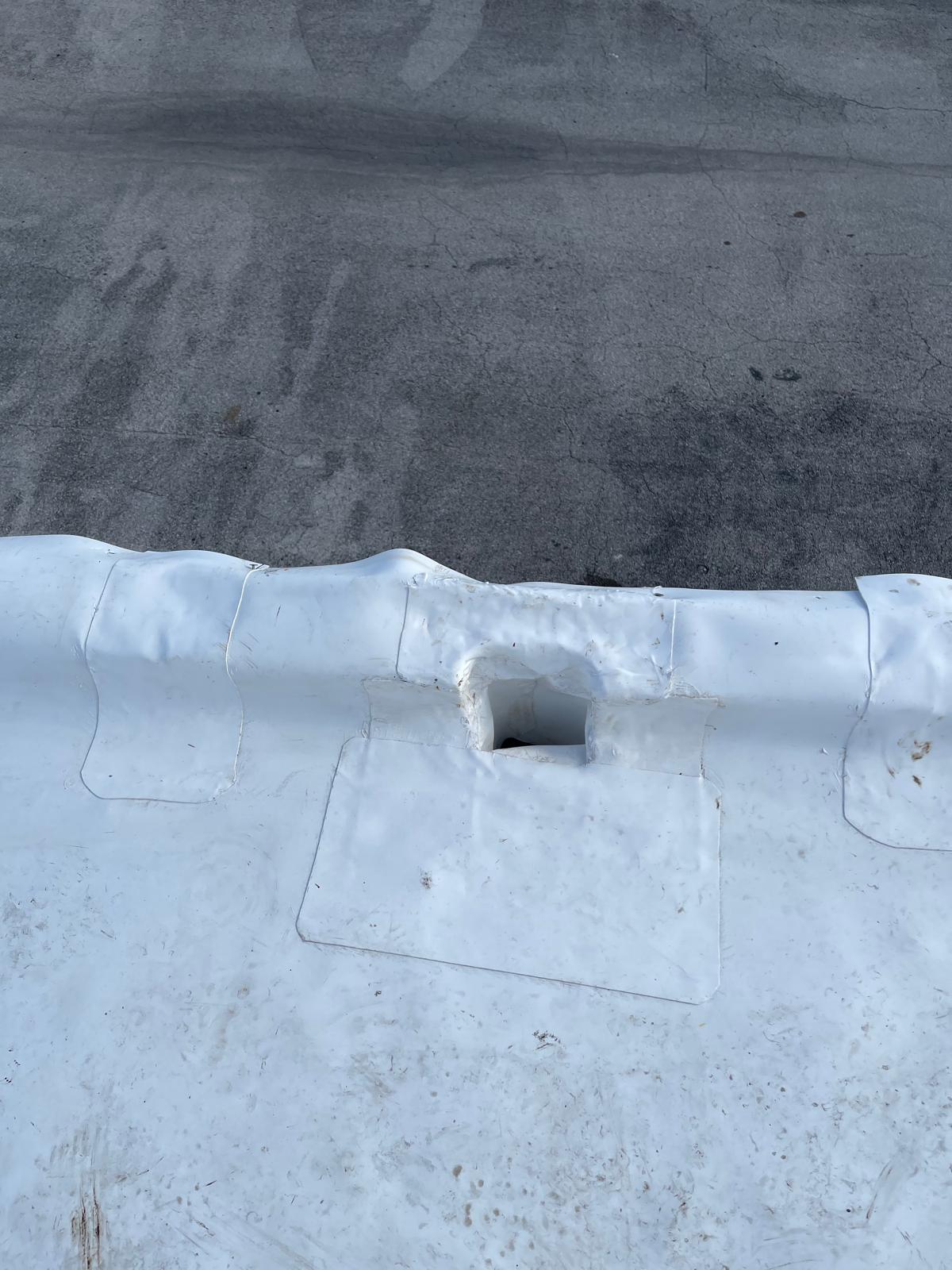 A white rooftop membrane with a rectangular hole and visible patchwork near the edge.